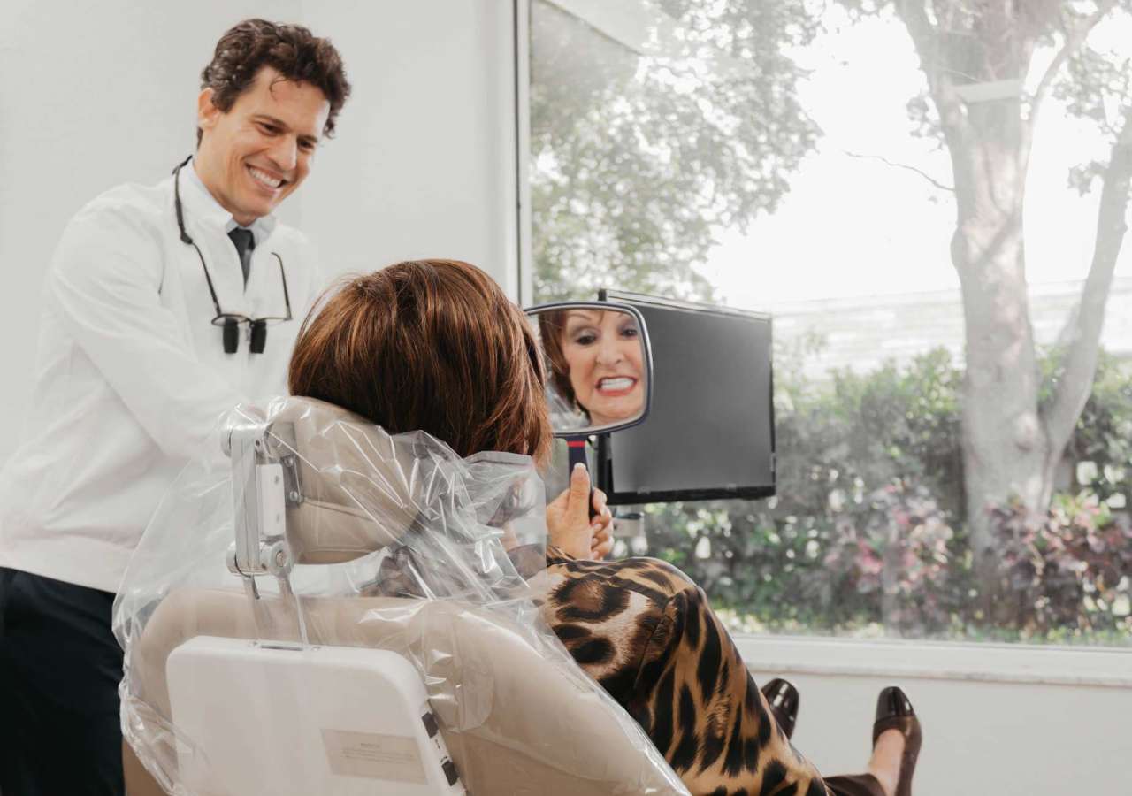 A patient seeing her new smile in the mirror with Dr. Macedo